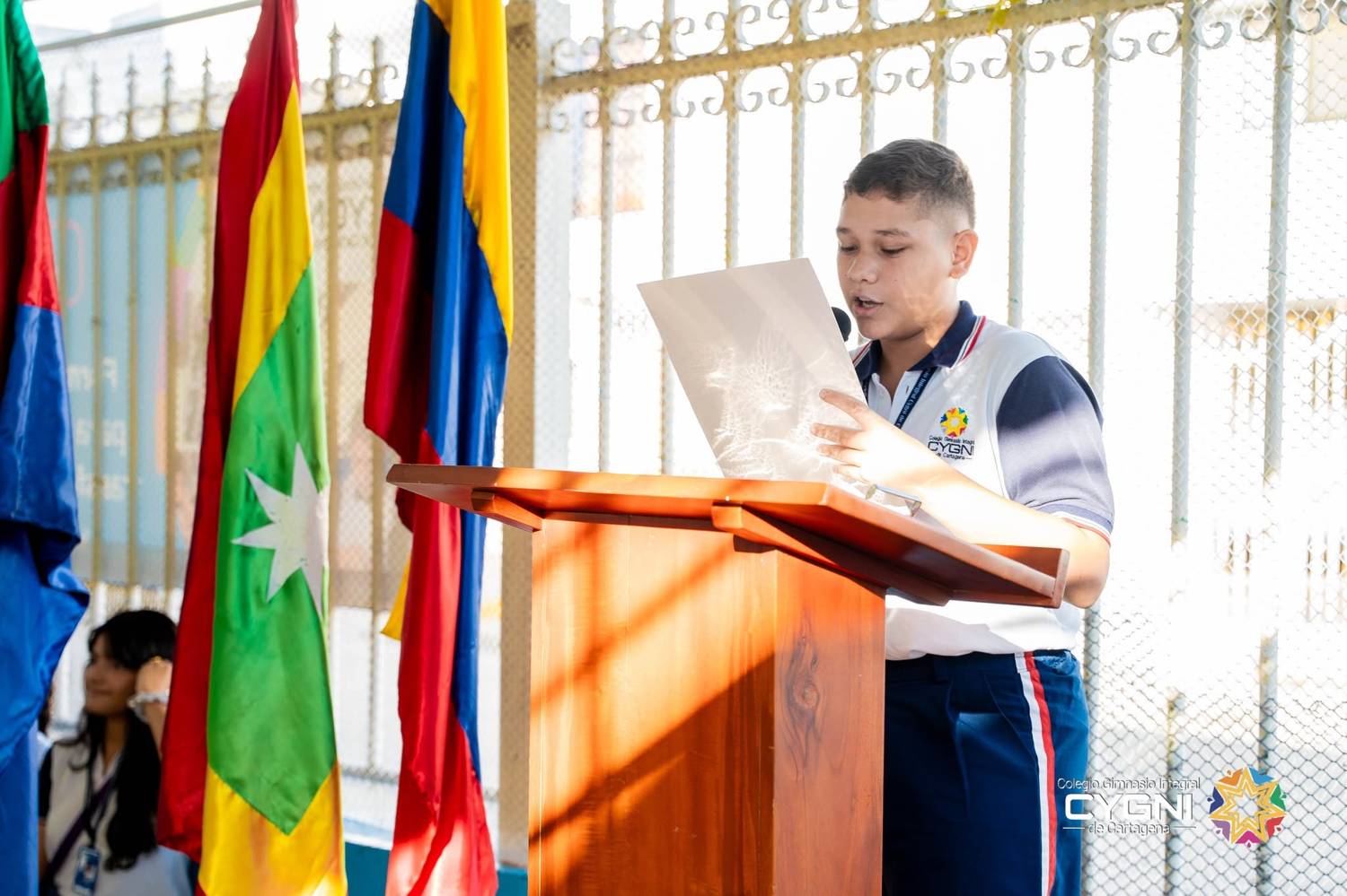 Estudiante leyendo en el atril junto a las banderas